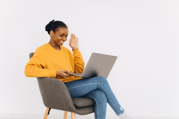 Donna afroamericana che si siede sulla sedia con il computer portatile e che comunica la videochiamata
