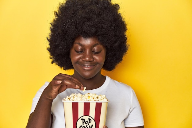 Donna afroamericana che tiene il concetto di cinema popcorn su sfondo giallo