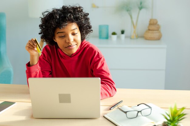 Donna afroamericana che usa un portatile per fare acquisti online pagando con una carta di credito d'oro.