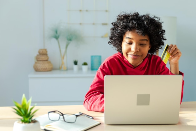 Donna afroamericana che usa un portatile per fare acquisti online pagando con una carta di credito d'oro.