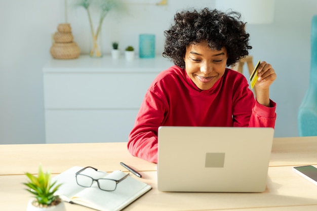 Donna afroamericana che utilizza il computer portatile per lo shopping online pagando con carta di credito gold