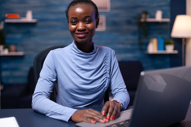 Donna afroamericana che utilizza la tecnologia lavorando a distanza da casa di notte alla scadenza. Imprenditore nero seduto sul posto di lavoro personale scrivendo sulla tastiera.