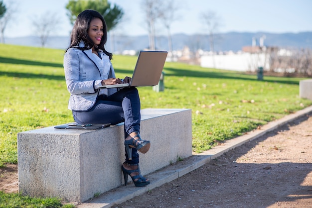 Donna afroamericana che utilizza un computer portatile in un parco all'aperto