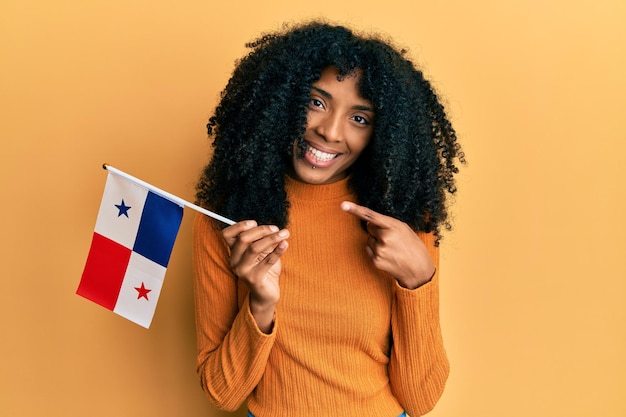 Donna afroamericana con capelli afro che tiene bandiera panama sorridente felice indicando con mano e dito