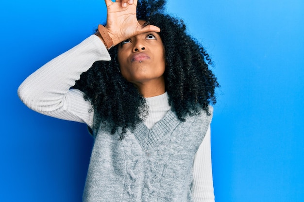 Donna afroamericana con i capelli afro che indossa un maglione invernale casual prendendo in giro le persone con le dita sulla fronte facendo un gesto da perdente beffardo e offensivo