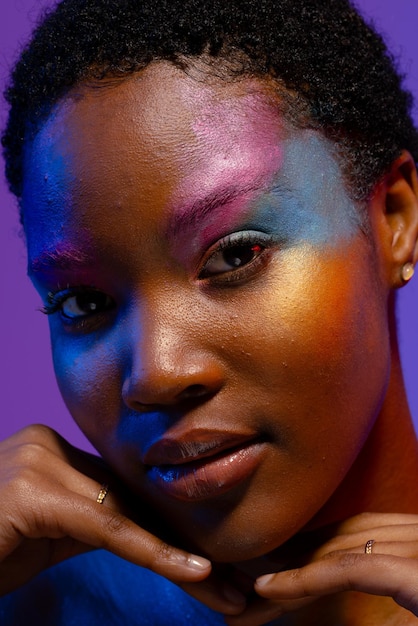 donna afroamericana con i capelli corti trucco colorato e le mani sotto il mento