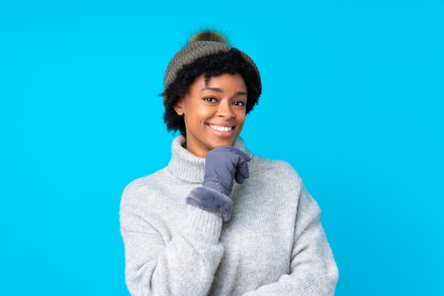 Donna afroamericana con il cappello di inverno sopra la parete blu isolata