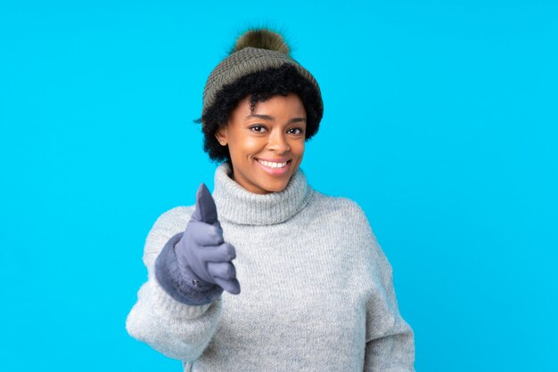 Donna afroamericana con il cappello di inverno sopra la parete blu isolata