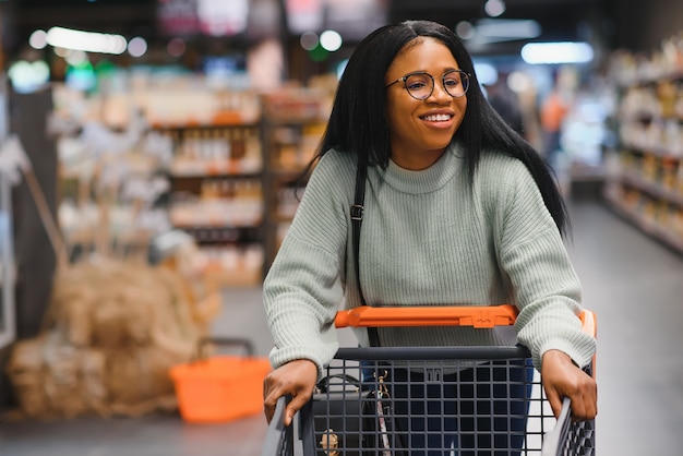 Donna afroamericana con il carrello del carrello della spesa nel negozio del supermercato.