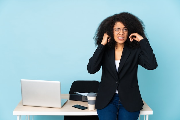 Donna afroamericana di affari che lavora nel suo posto di lavoro frustrata e che copre le orecchie