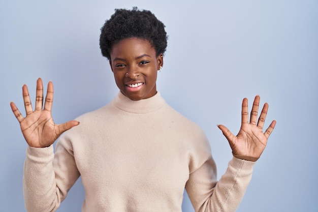Donna afroamericana in piedi su sfondo blu che mostra e indica con le dita numero dieci mentre sorride fiducioso e felice.