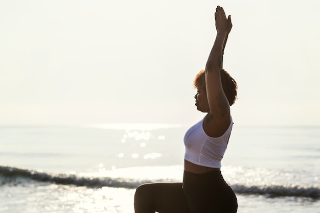 Donna afroamericana praticando yoga in spiaggia