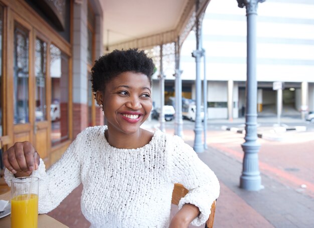 Donna afroamericana sorridente che si siede al ristorante all&#39;aperto