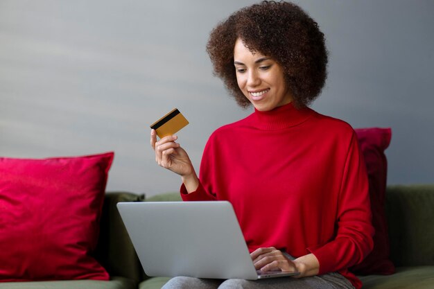 Donna afroamericana sorridente che tiene la carta di credito che fa acquisti online ordinando cibo sul sito web