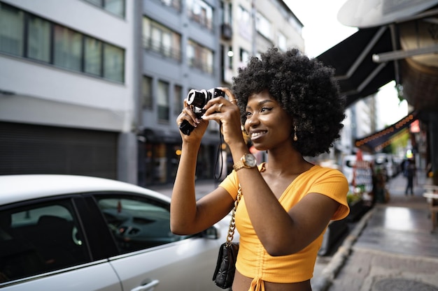 Donna afroamericana sorridente che utilizza una fotocamera professionale in una strada