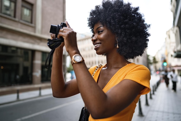 Donna afroamericana sorridente che utilizza una fotocamera professionale in una strada