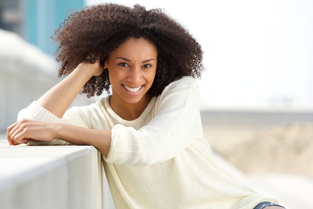 Donna afroamericana sorridente con capelli ricci che si siedono all&#39;aperto