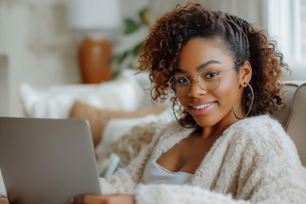 donna afroamericana sorridente seduta sul divano usando un portatile per lavoro remoto o concetto di studio