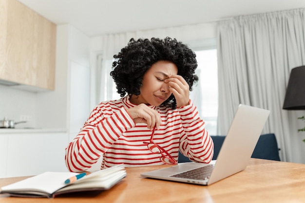 Donna afroamericana stanca e frustrata che lavora online da casa con dolore agli occhi Stress da mal di testa