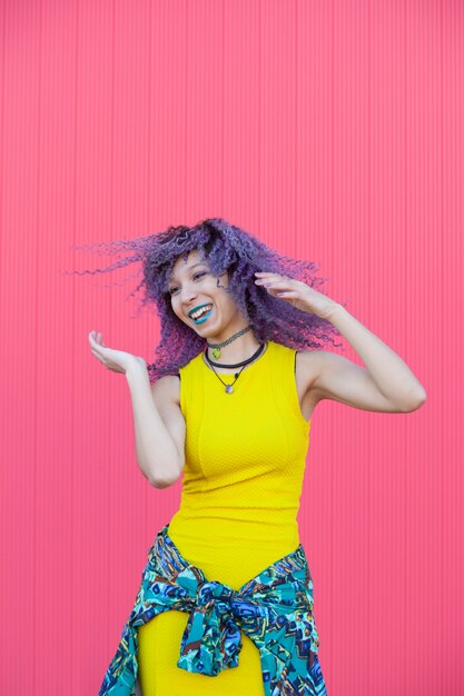 Donna afroamericana teenager felice che balla con un vestito giallo e capelli viola