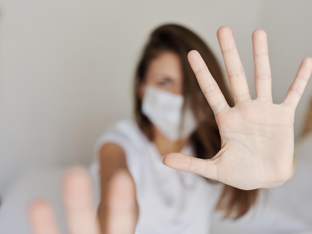 Donna aggressiva con una maschera medica copre la telecamera con le mani su uno sfondo leggero coronavirus pandemico foto di alta qualità