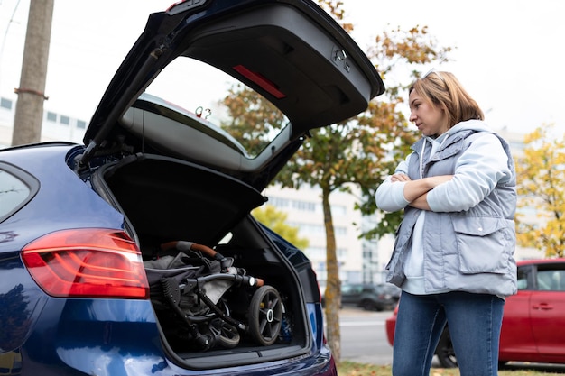 Donna al bagagliaio aperto di un'auto con un passeggino all'interno