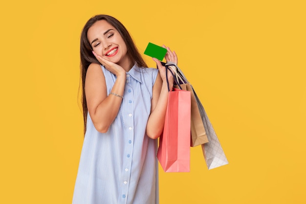 Donna alla moda anni '20 in abito con lunghi capelli castani che sorride mentre tiene in mano diversi pacchetti della spesa e carta nelle mani isolate su sfondo giallo