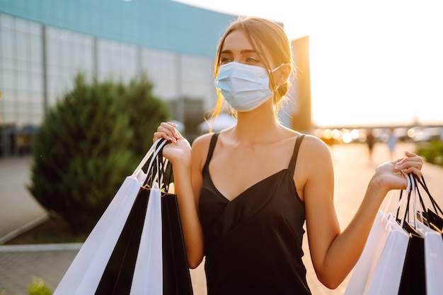 Donna alla moda che indossa maschera medica protettiva con borse della spesa al tramonto.