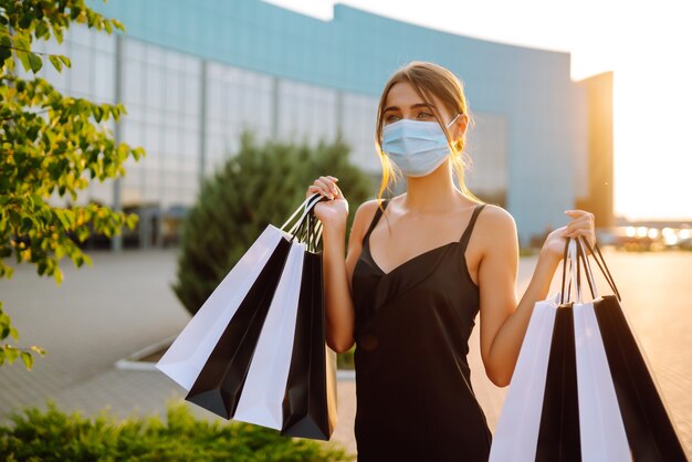 Donna alla moda che indossa maschera medica protettiva con borse della spesa al tramonto.