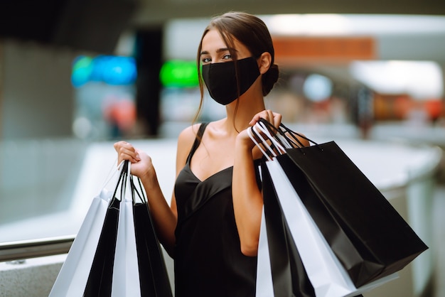 Donna alla moda che indossa maschera medica protettiva con borse della spesa nel centro commerciale.