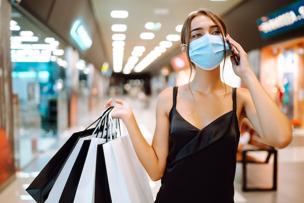 Donna alla moda che indossa maschera medica protettiva con borse della spesa nel centro commerciale.