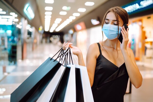 Donna alla moda che indossa maschera medica protettiva con borse della spesa nel centro commerciale.