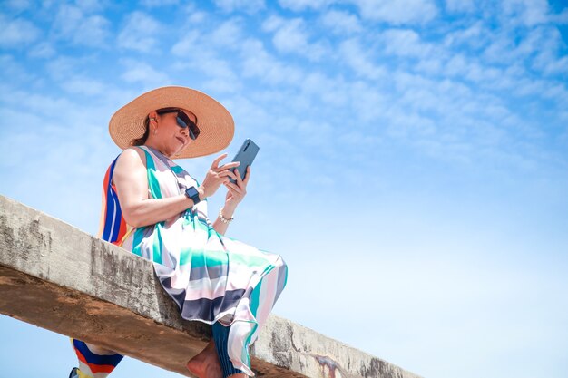 Donna alla moda che indossa un abito lungo colorato e tiene in mano uno smartphone per scattare foto.