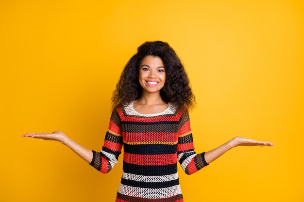 Donna alla moda con acconciatura afro in posa contro il muro arancione