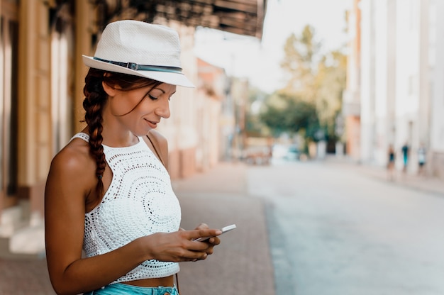 Donna alla moda con cappello utilizzando il telefono al di fuori.