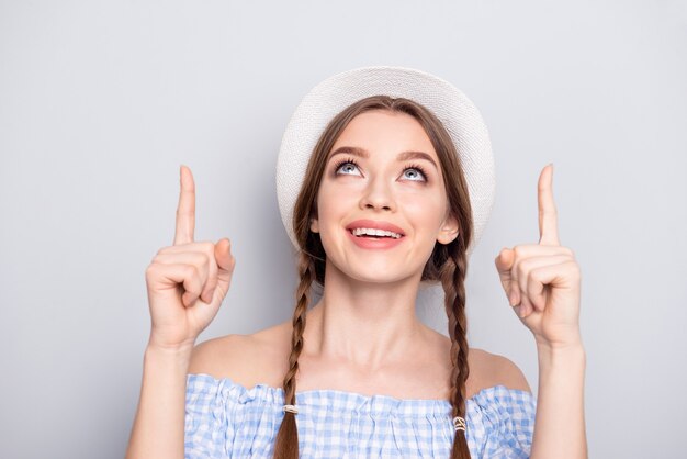 Donna alla moda con trecce e cappello in posa contro il muro bianco