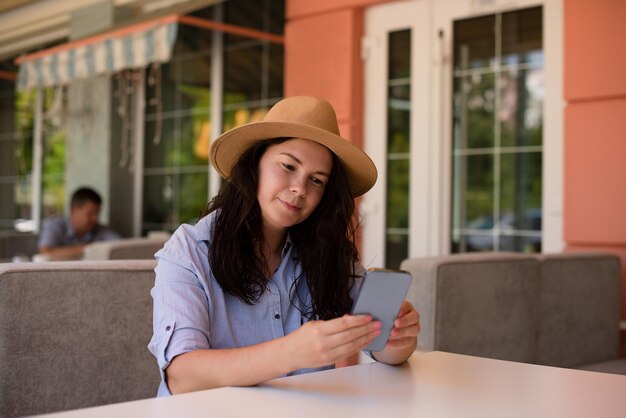 Donna alla moda in cappello con smartphone che fa videochiamate e sorride