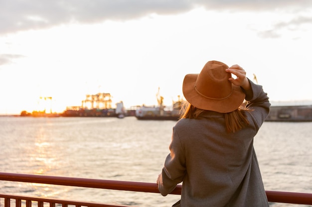 Donna alla moda in cappello di feltro e cappotto all'alba in mare