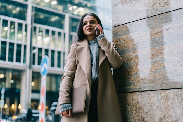 Donna alla moda in cappotto con il taccuino che parla sullo smartphone