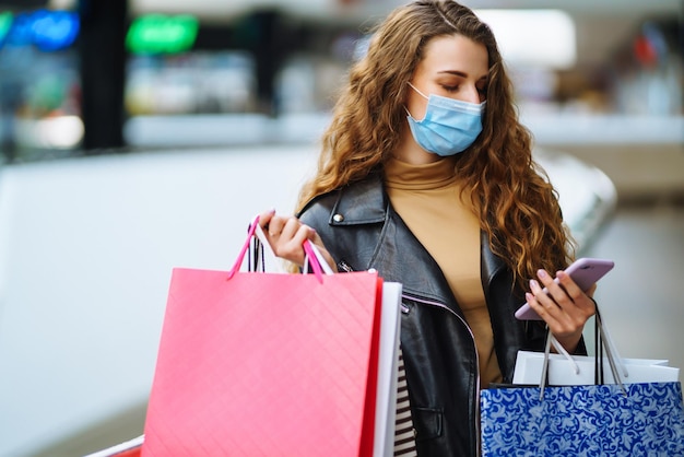 Donna alla moda in maschera medica protettiva con borsa della spesa che usa il suo telefono Stile di moda Blackfriday