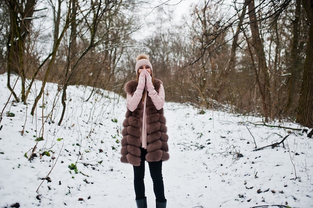 Donna alla moda in pelliccia e copricapo nella foresta invernale.