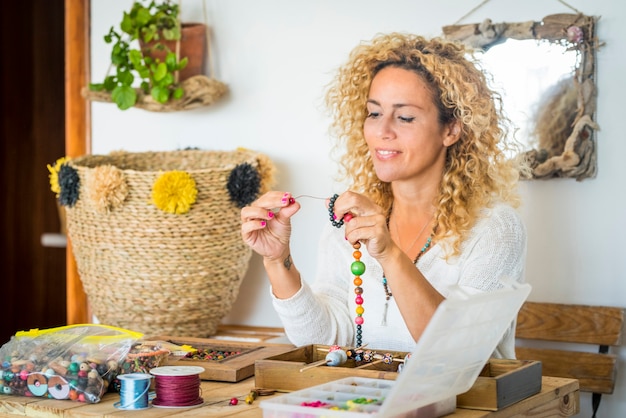 Donna allegra a casa che fa bracciali e collane con perline colorate