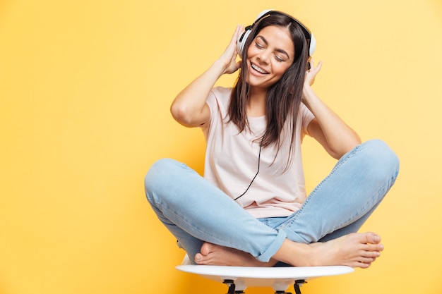 Donna allegra che ascolta musica in cuffia sul muro giallo