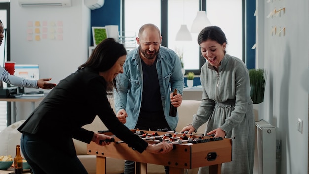 Donna allegra che balla dopo aver vinto la partita al biliardino in ufficio. Colleghi che giocano a calcio e si godono attività divertenti dopo il lavoro. Colleghi multietnici che bevono bevande e snack