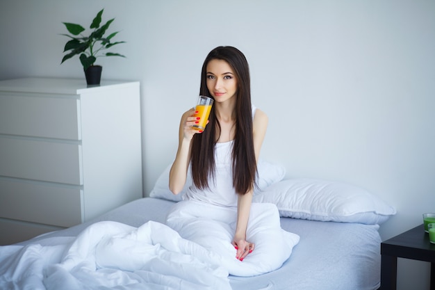 Donna allegra che beve un succo d'arancia che si siede sul suo letto a casa