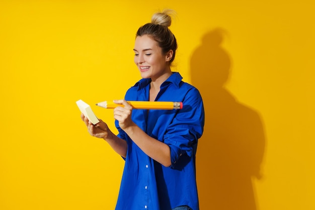 Donna allegra che indossa una camicia blu che tiene una matita gigante su sfondo giallo