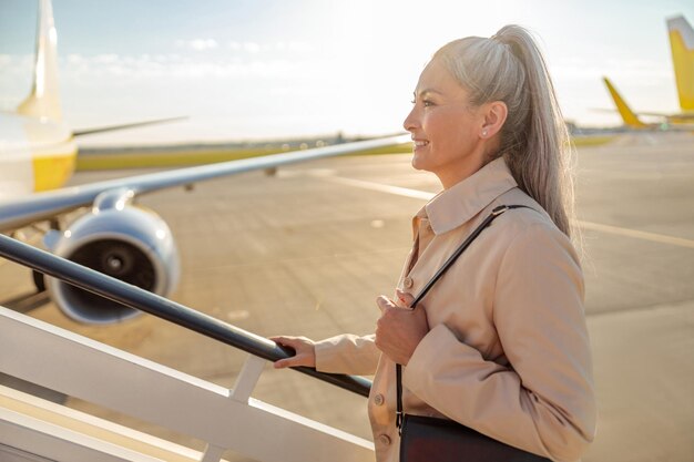 Donna allegra che sale le scale dell'aeroplano all'aeroporto