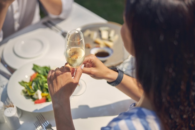 donna allegra che tiene in mano un bicchiere di champagne mentre è seduta al tavolo da pranzo