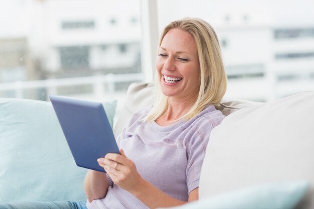 Donna allegra che utilizza computer tablet sul divano