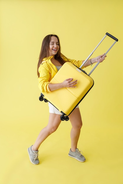 Donna allegra con borsa da viaggio trolley in piedi in studio